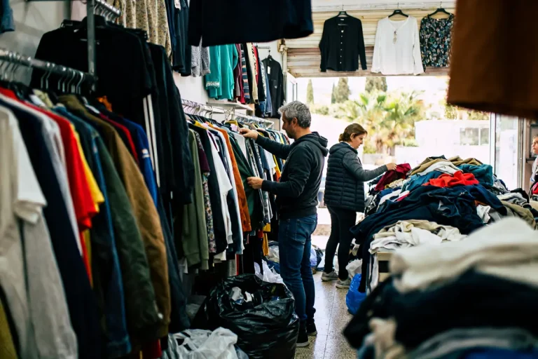 Personnes explorant les vêtements dans Les friperies du sud avec étagères et piles de vêtements
